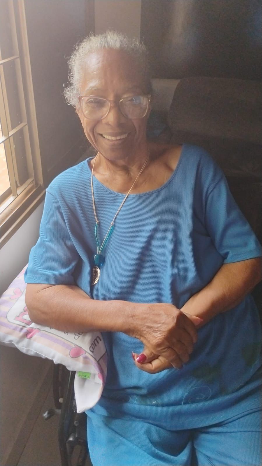 Senhora Alexandrina, sorridente vestindo blusa azul e colar